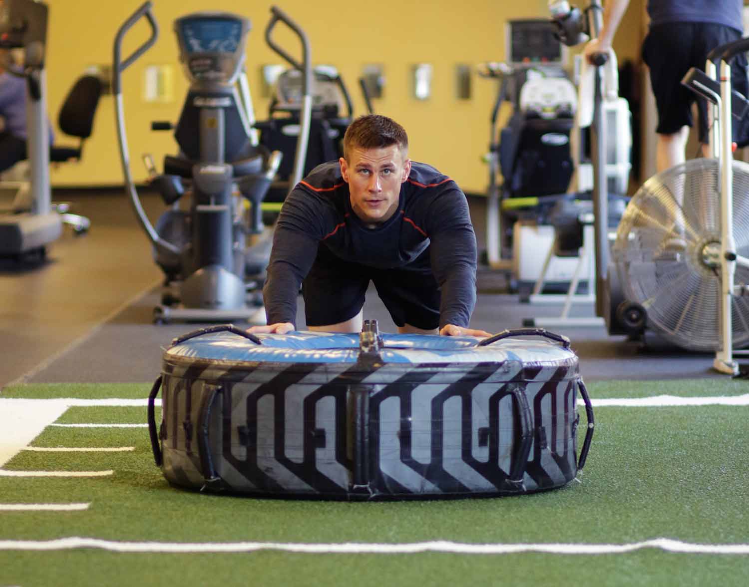 Man pushing a tire across the turf in the Performance Training Center.