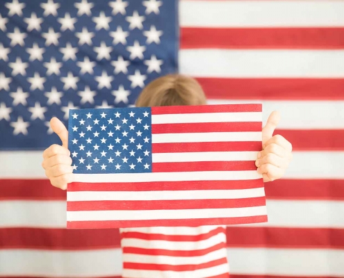 Young girl holding an American flag in front of an American flag backdrop.