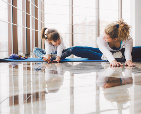 Woman and girl stretching together in yoga studio.