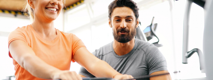 Image of a woman using a rowing machine with a personal trainer.