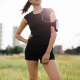 Cropped shot of fitness woman standing in urban park wearing sportswear and mobile phone armband. Female model in sportswear with earphones listening to music during workout break.