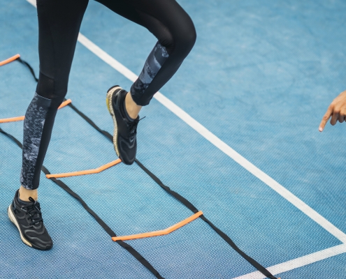 Young woman exercising with personal fitness coach using agility ladder. Agility skill improvement.