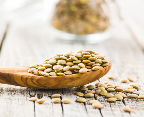 Uncooked dried lentil in wooden spoon.