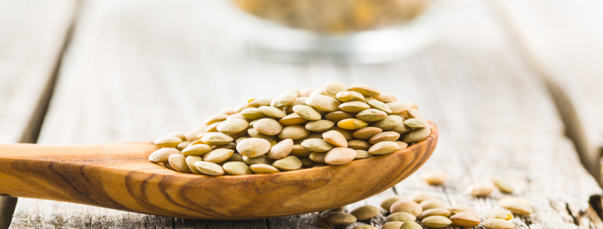 Uncooked dried lentil in wooden spoon.