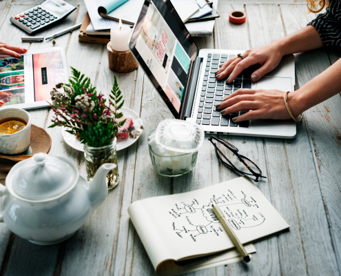 women at large table with computers, tea pot, journals