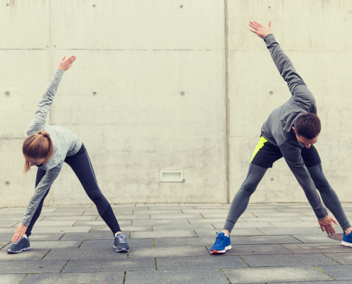 Man and woman outside in running gear stretching