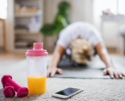 Woman stretching on the floor of her living room with weights and phone nearby.