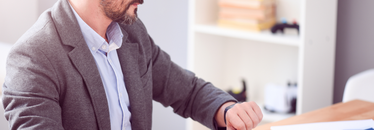 Man sitting at work desk looking at his watch.