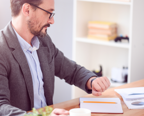 Man sitting at work desk looking at his watch.