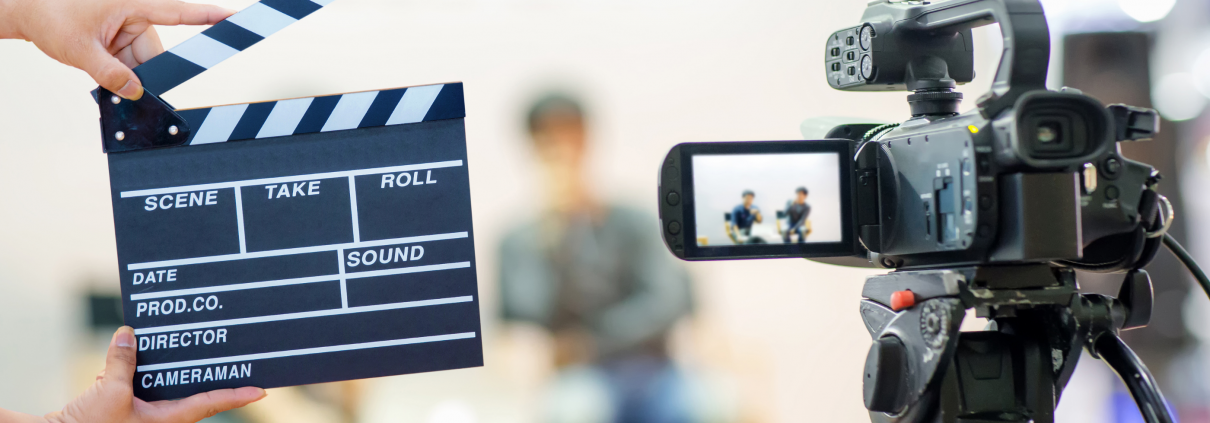Photo of clapboard and digital camera in front of two people sitting