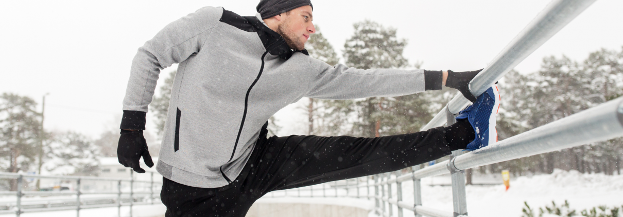 Man in his 30s stretching outside in the snow after a run