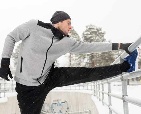Man in his 30s stretching outside in the snow after a run