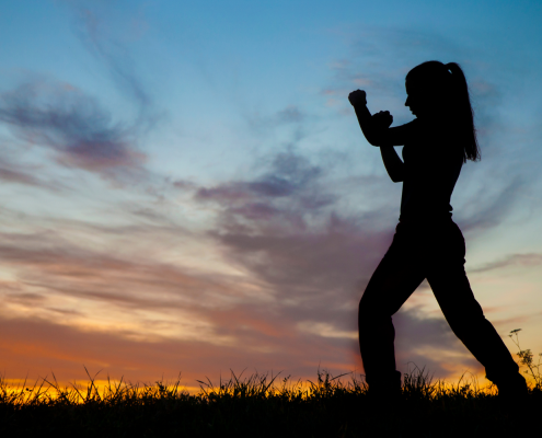 Outline of a woman at sunset with fists up in fighting stance