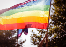 Person holding up a rainbow Pride flag outside