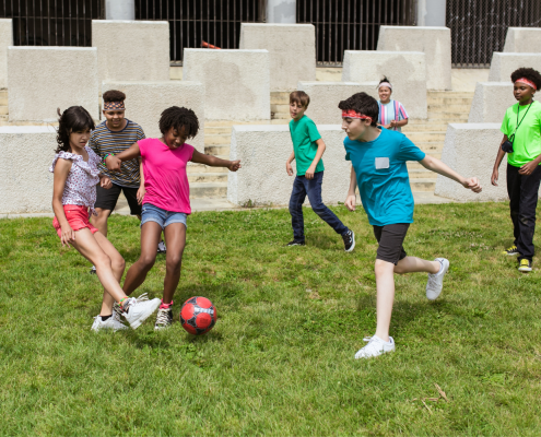 Kids playing soccer outside in the grass.