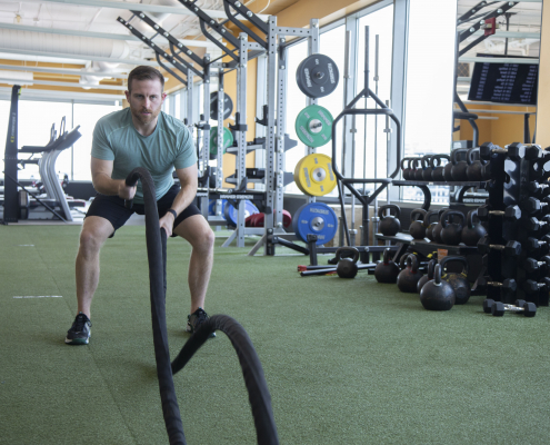 Man using battle ropes on turf inside a gym