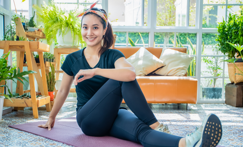 Girl stretching on a yoga mat in front of a couch and potted plants.