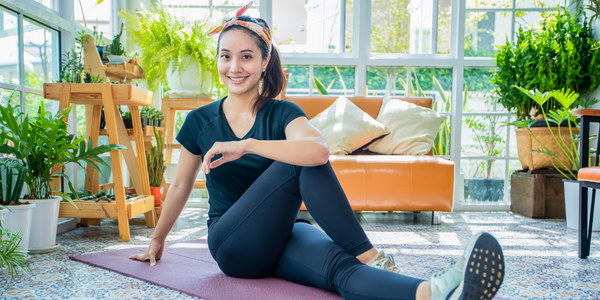 Girl stretching on a yoga mat in front of a couch and potted plants.