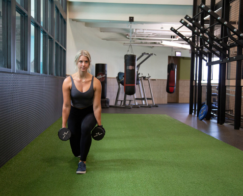 photo of woman on indoor turf in a lunging position with dumbbels