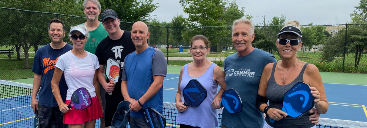 Group of people smiling and standing together in front of a pickleball net.