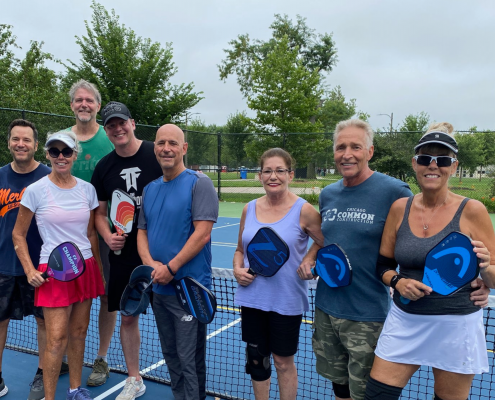 Group of people smiling and standing together in front of a pickleball net.