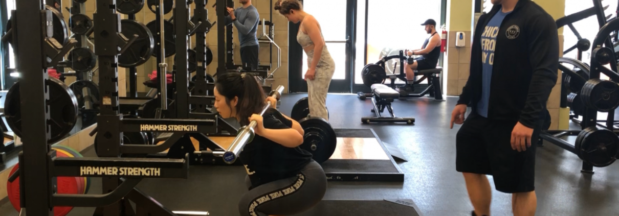 A woman at a squat rack with her trainer