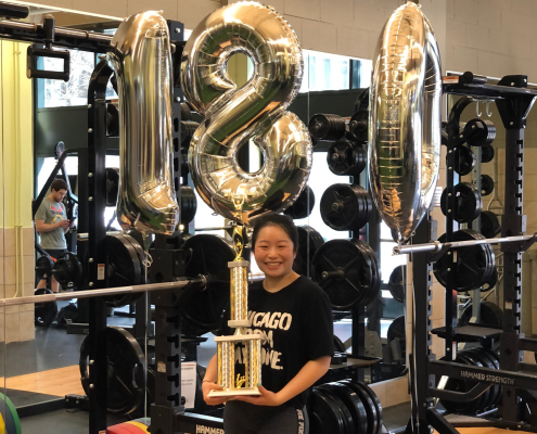 Emily With Balloons and A Trophy standing in front of a squat rack