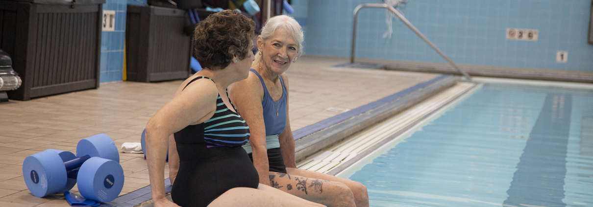 Two older women sitting on the edge of a pool