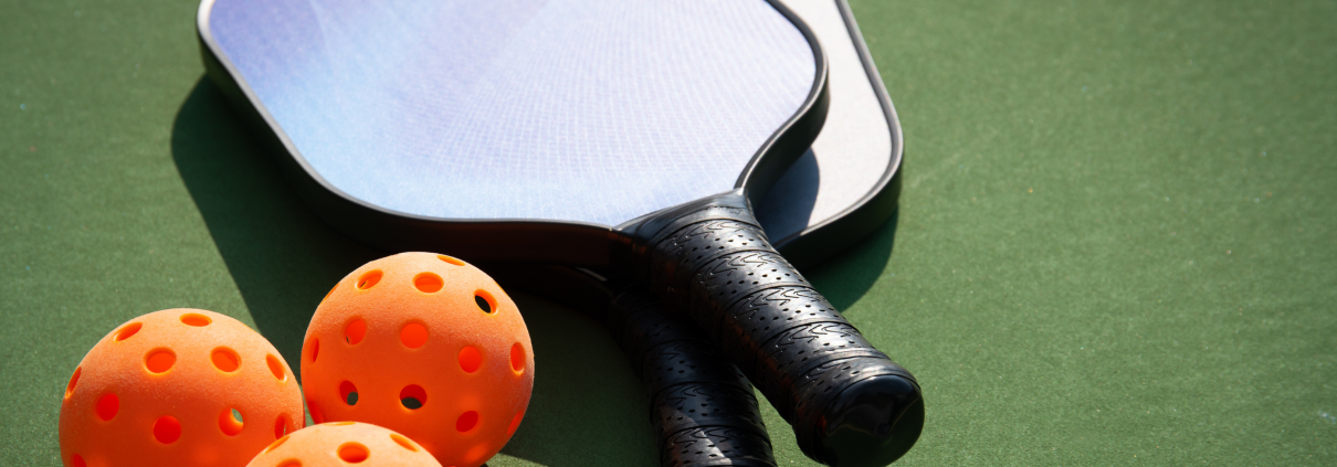 Three orange pickleballs and two paddles set on a court