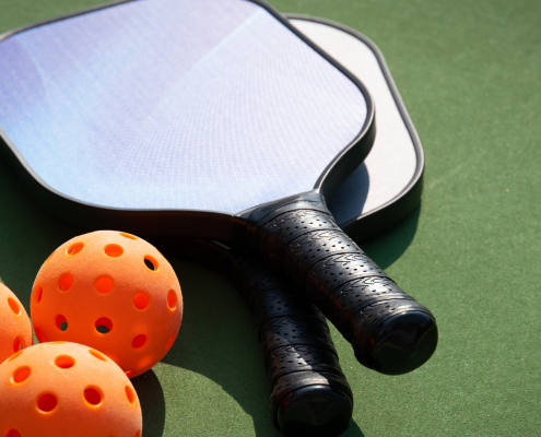 Three orange pickleballs and two paddles set on a court