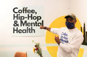 Man standing in front of a wall that says Coffee Hip Hop and Mental Health