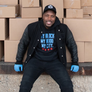 Man sitting in front of boxes wearing a My Block My Hood My City sweatshirt