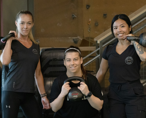 3 women holding kettlebells and smiling at the camera