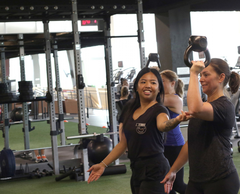 2 women working out on a turfed fitness area with kettlebells