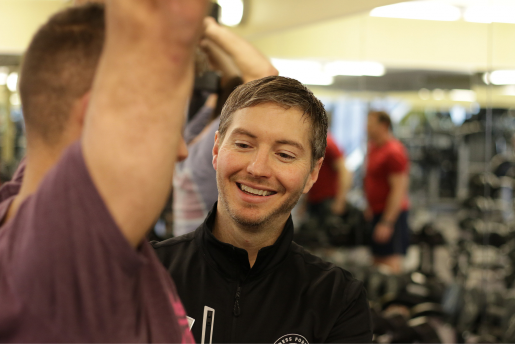 Personal trainer assisting male member during lift.